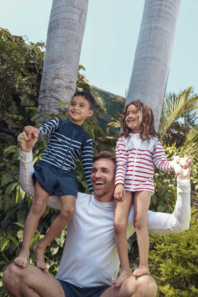Homme portant un t-shirt anti-UV blanc, avec deux enfants en maillots à rayures, idéal pour jouer en extérieur.